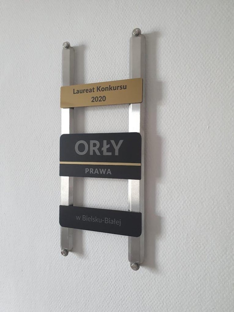 Tablica z napisem 'Orły Prawa' i informacją o laureacie konkursu 2020 w Bielsku-Białej, przymocowana do ściany, prezentująca nagrodę prawniczą.