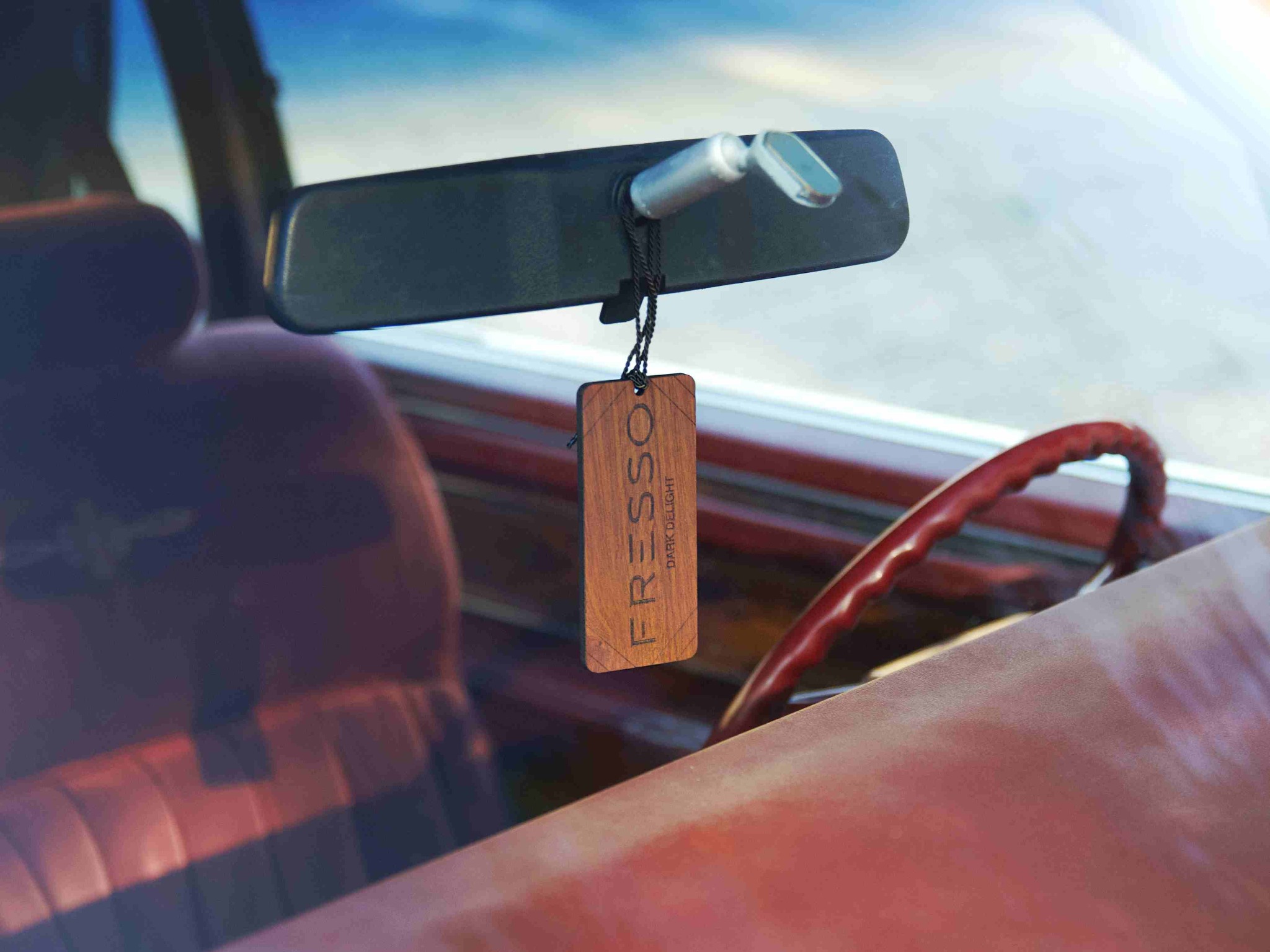 Drewniany zapach samochodowy marki Fresso, model Dark Delight, zawieszony na lusterku wstecznym wewnątrz auta z czerwoną kierownicą i tapicerką.