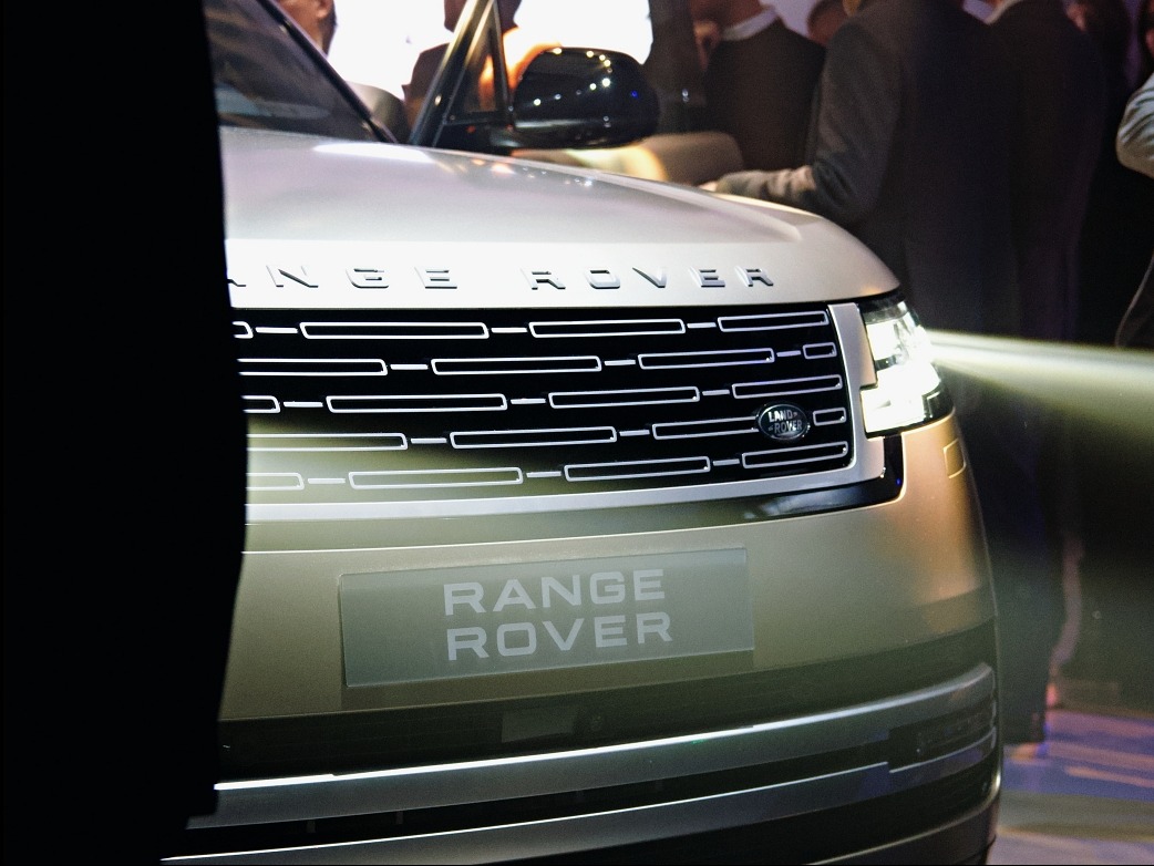 Szczegółowe ujęcie przodu złotego Range Rovera z włączonym reflektorem, prezentowanego na tle tłumu podczas wydarzenia motoryzacyjnego.