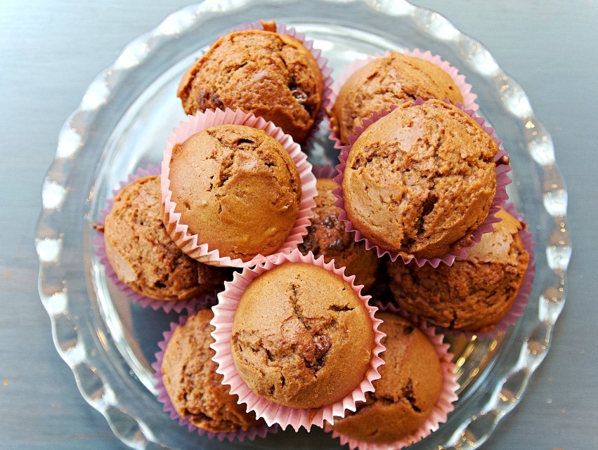 Aromatyczne, czekoladowe babeczki w różowych papilotkach, ułożone na szklanym talerzu z falistym brzegiem, na szarym tle. Widok z góry, naturalne światło.