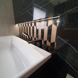 Usługi Hydrauliczne i Wykończeniowe Krzysztof Asztemborski - Nowoczesna łazienka z białą umywalką, czarną armaturą i dekoracyjną ścianą z podświetlonymi elementami drewnianymi na tle czarnego marmuru.