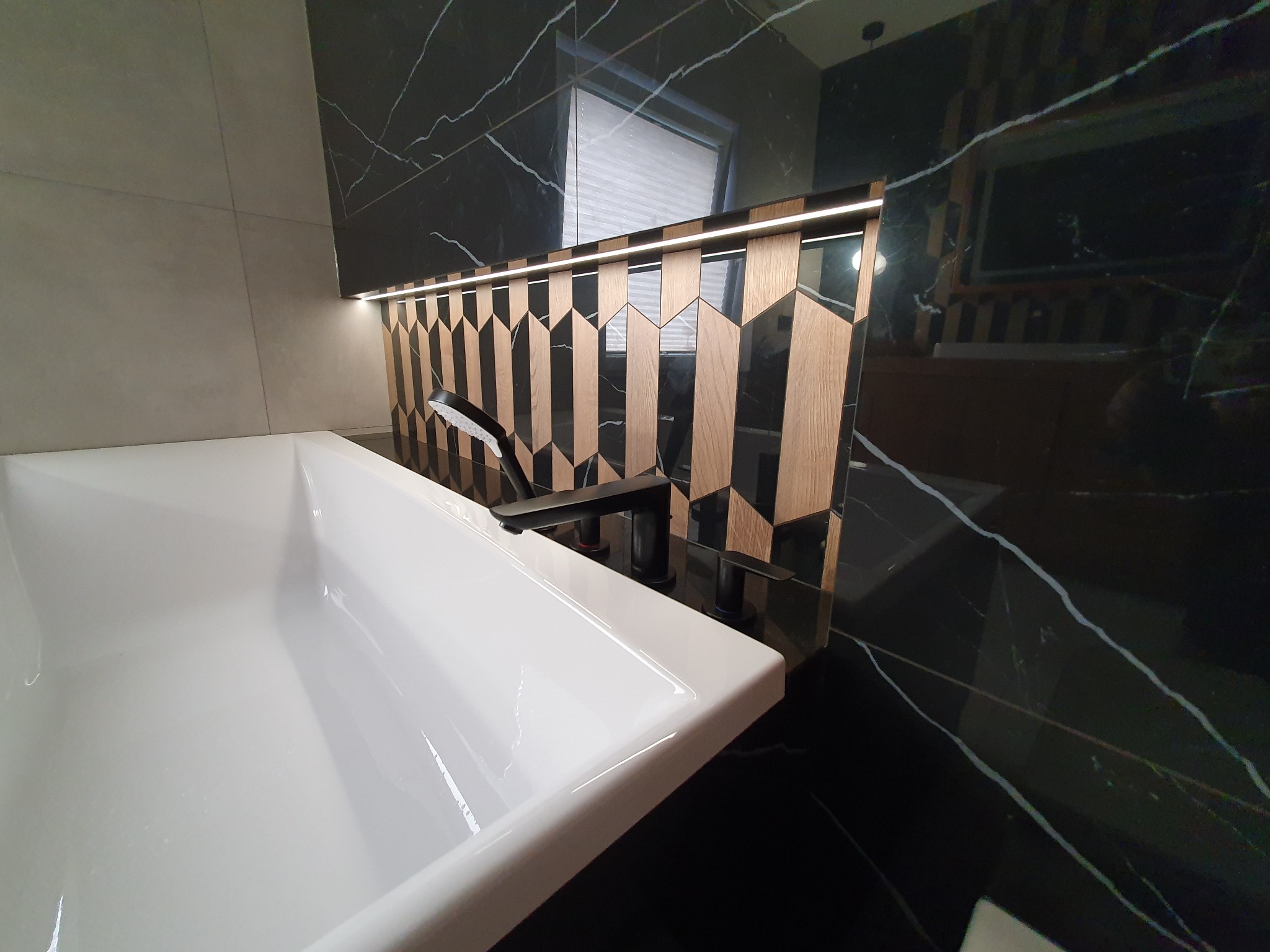 Nowoczesna łazienka z białą umywalką, czarną armaturą i dekoracyjną ścianą z podświetlonymi elementami drewnianymi na tle czarnego marmuru.