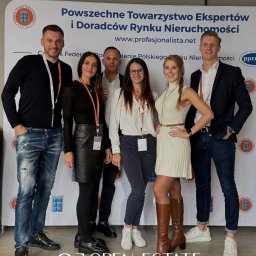 Mateusz Dąbkowski Open Estate - Zespół Open Estate Nieruchomości pozuje na tle baneru Powsz. Towarzystwa Ekspertów i Doradców Rynku Nieruchomości. Widoczne logo firmy na dole zdjęcia.