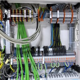 Pod-napięciem - Rozdzielnica elektryczna z precyzyjnie ułożonymi przewodami w różnych kolorach, widoczne listwy zaciskowe i moduły zabezpieczeń. Estetyczne i profesjonalne wykonanie instalacji.