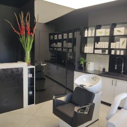 Trychologia Bednarek - Nowoczesny gabinet trychologiczny: fotel do zabiegów na włosy z umywalką, recepcja z kwiatami, półki z kosmetykami. Stonowana kolorystyka, minimalistyczny design.