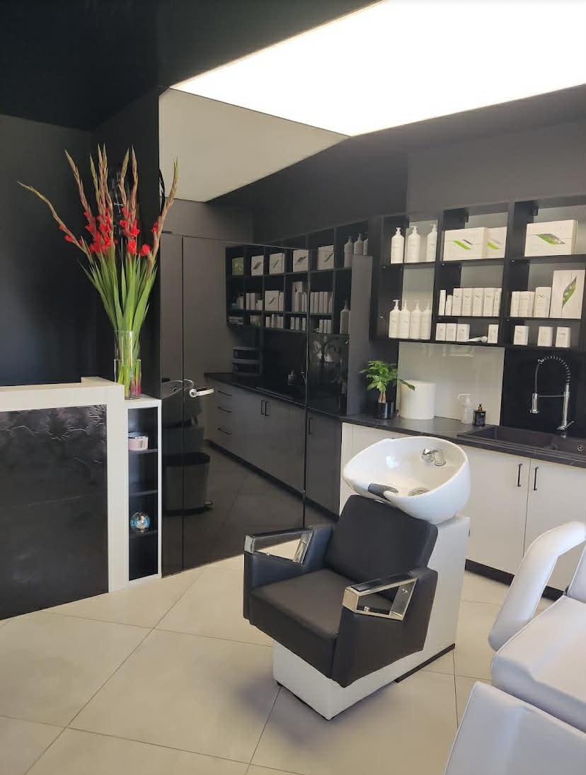 Nowoczesny gabinet trychologiczny: fotel do zabiegów na włosy z umywalką, recepcja z kwiatami, półki z kosmetykami. Stonowana kolorystyka, minimalistyczny design.