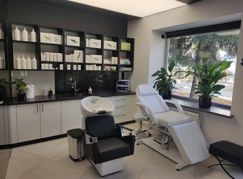 Nowoczesny gabinet trychologiczny: białe meble, fotel z umywalką, leżanka kosmetyczna przy oknie z roślinami. Minimalistyczny wystrój, profesjonalne wyposażenie.