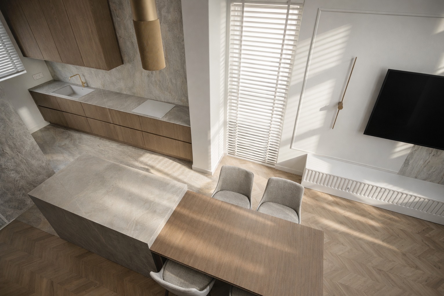 Nowoczesna kuchnia z wyspą i drewnianymi szafkami, widziana z góry. Parkiet w jodełkę, minimalistyczny design, stonowana kolorystyka, rolety okienne, telewizor na ścianie.