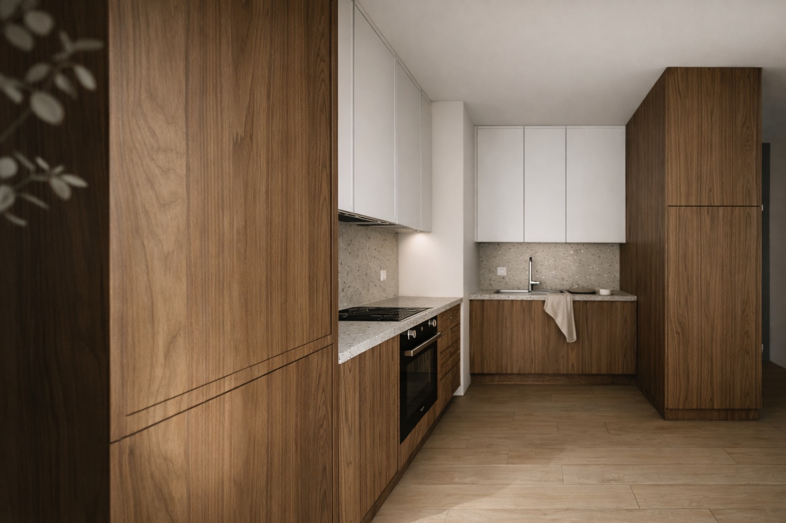 Nowoczesna kuchnia z drewnianymi frontami szafek dolnych i białymi górnymi, blatem w kolorze lastryko i drewnianą podłogą. Minimalistyczny design z subtelnym oświetleniem.