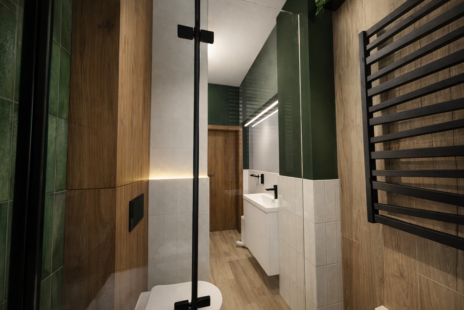 Nowoczesna łazienka z drewnianymi i zielonymi akcentami, kabiną prysznicową typu walk-in i czarnym grzejnikiem drabinkowym. Oświetlenie LED podkreśla detale.