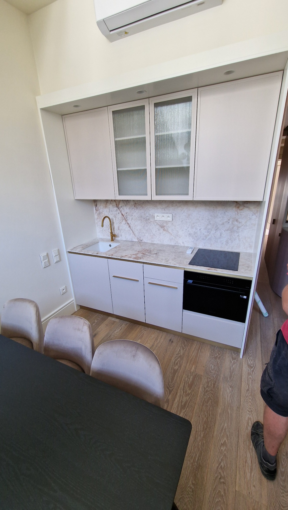 Jasna kuchnia z marmurowym blatem i złotą armaturą. Widoczne krzesła i fragment stołu. Minimalistyczny design z elementami luksusu.