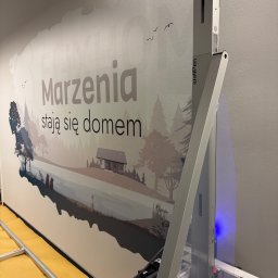 WallKing Łukasz Żugaj - Ściana z nadrukiem krajobrazu wykonanym przez urządzenie WallPen. Napis: Marzenia stają się domem. Widoczne elementy urządzenia drukującego.