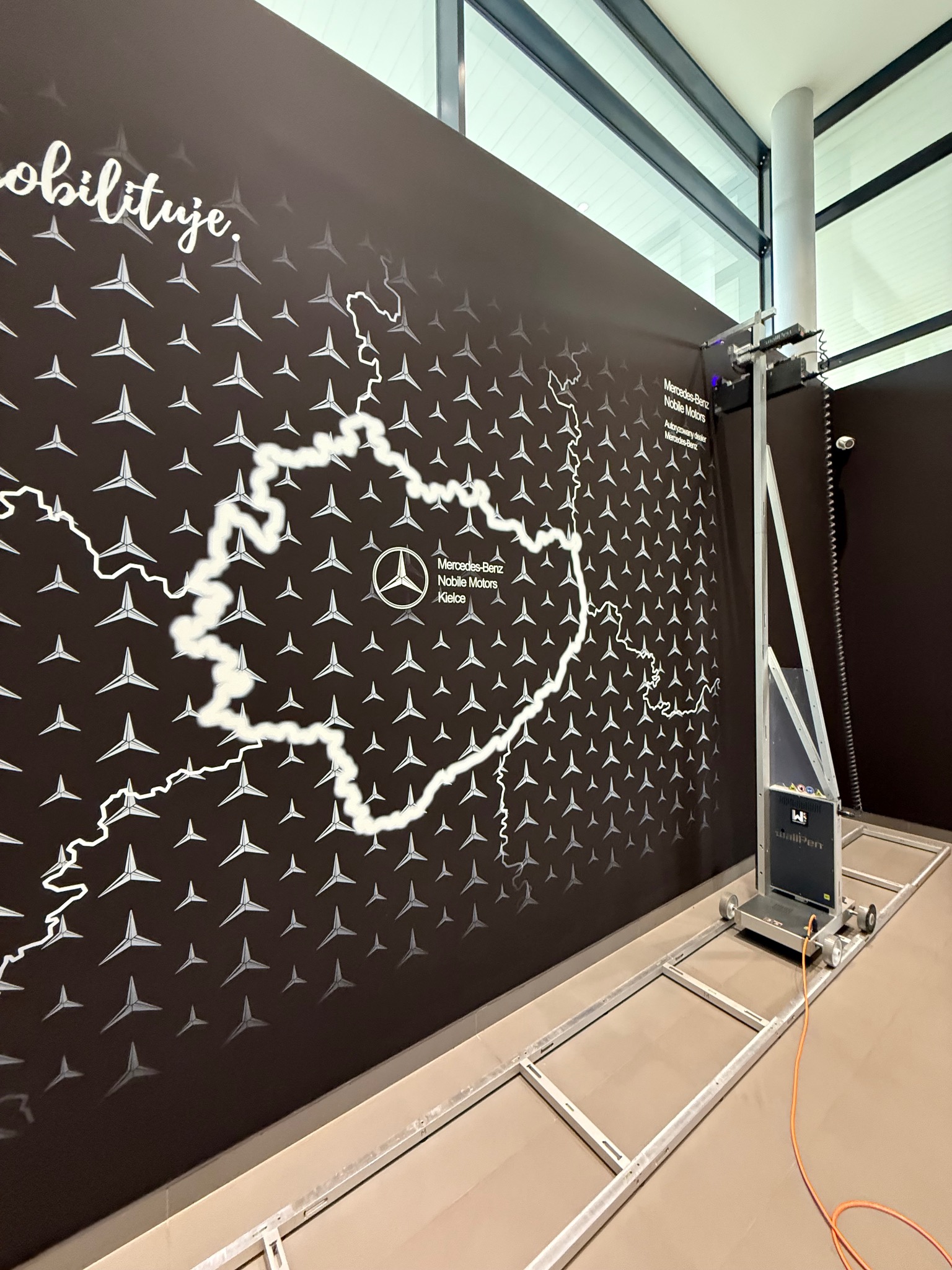WallPen drukuje na ścianie mapę Polski z logo Mercedes-Benz w salonie Nobile Motors Kielce. Automat malarski na szynach, nowoczesny design.