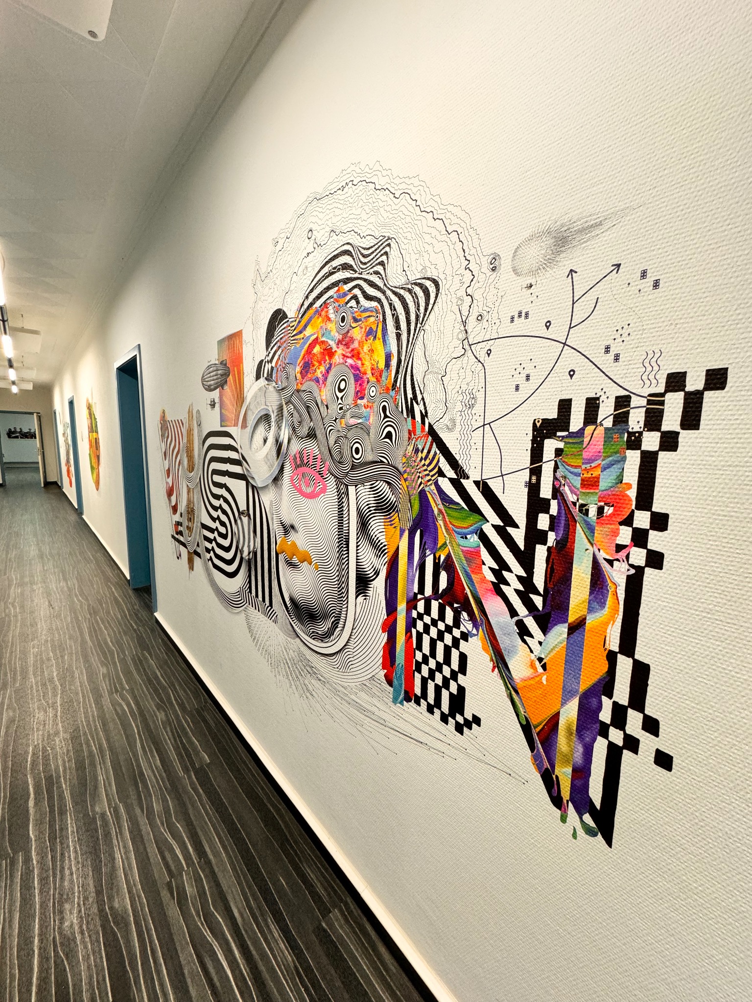 Abstrakcyjna grafika ścienna w korytarzu biurowym. Kolorowe i czarno-białe elementy tworzą unikalny wzór, dodając artystyczny akcent do wnętrza.