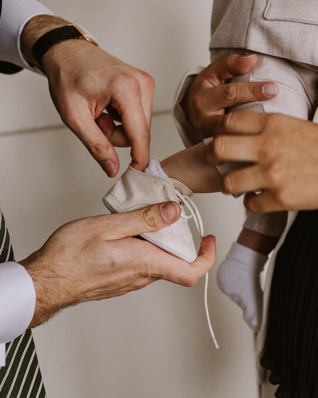 Drobne buciki w dłoniach mężczyzny, przygotowywane do założenia na małą stopę dziecka w białej skarpetce. Ujęcie z bliska, ciepłe barwy, delikatne światło.