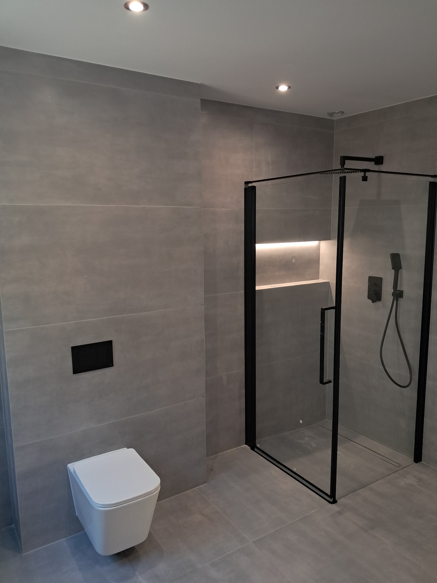 Nowoczesna łazienka we Wrocławiu z szarymi płytkami, kabiną prysznicową z czarnymi ramami i podwieszaną toaletą. Minimalistyczny design, oświetlenie LED wnęki.