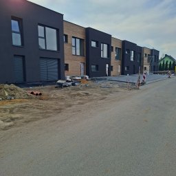 Mmam - Nowoczesne domy szeregowe z czarną i drewnianą elewacją w trakcie budowy. Widoczne materiały budowlane i rusztowania. Słoneczny dzień.