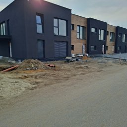 Mmam - Nowoczesne domy w zabudowie szeregowej z czarną elewacją i elementami drewnianymi, w trakcie prac wykończeniowych. Widoczne materiały budowlane i przygotowany teren.