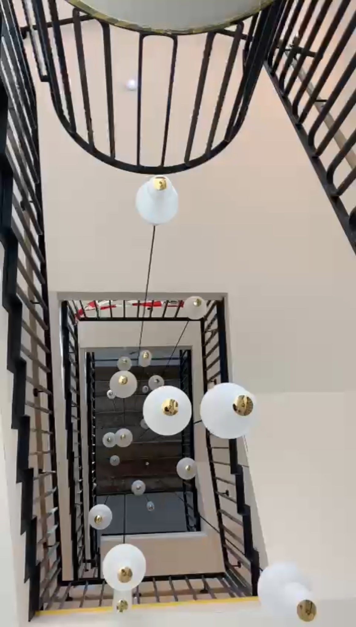 Nowoczesna klatka schodowa z czarnymi balustradami i oryginalną, wiszącą lampą z białymi kulami. Widok z góry na dół, podkreślający geometryczny układ schodów.