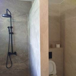 BUDREM OLHA MOROZ - Nowoczesna łazienka z kabiną typu walk-in, wykończona płytkami imitującymi marmur. Czarna armatura prysznicowa i toaleta w jasnej tonacji. Minimalistyczny design.
