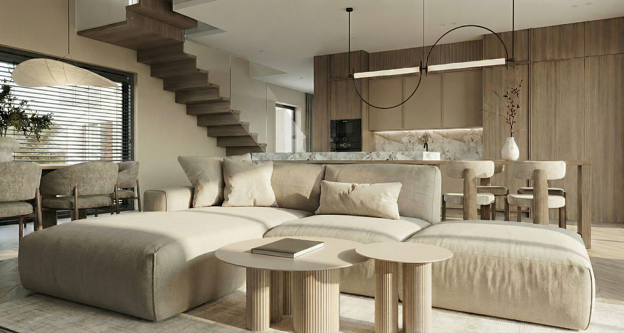 Jasne, przestronne wnętrze domu z drewnianymi schodami, beżową sofą i okrągłymi stolikami. Minimalistyczna kuchnia w tle, oświetlona nowoczesnymi lampami.