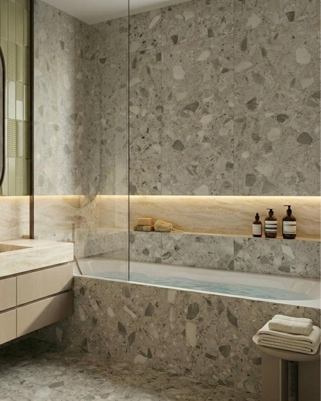 Nowoczesna łazienka z wanną obłożoną płytkami lastryko, szklana szyba oddzielająca strefę kąpielową, minimalistyczna umywalka i oświetlenie LED.