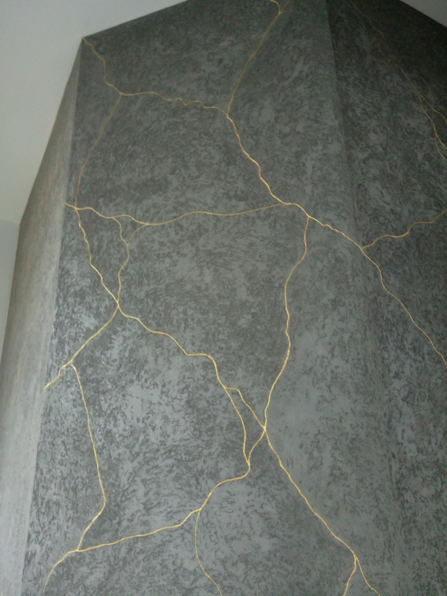 Dekoracyjna ściana w odcieniach szarości z efektem spękań wypełnionych złotem, imitującym japońską sztukę Kintsugi. Unikalna faktura i wykończenie narożnika.