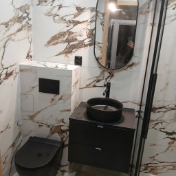 Volodymyr Mazepa - Wykończona łazienka z czarną armaturą: umywalka na szafce, wisząca toaleta i owalne lustro na tle marmurowych płytek. Nowoczesny design z akcentami czerni.