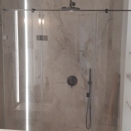 Marek Różański - Wykończona łazienka z kabiną prysznicową typu walk-in, marmurowe płytki na ścianach, oświetlenie LED. Widoczna toaleta i fragment szafki pod umywalkę.