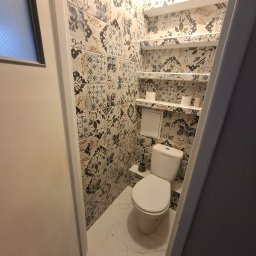 Rolling Tubes Bartłomiej Chmielewski - Wykończona toaleta z wzorzystymi płytkami na ścianach i podłodze. Biała ceramika, półki z akcesoriami. Widok z perspektywy wejścia do pomieszczenia.