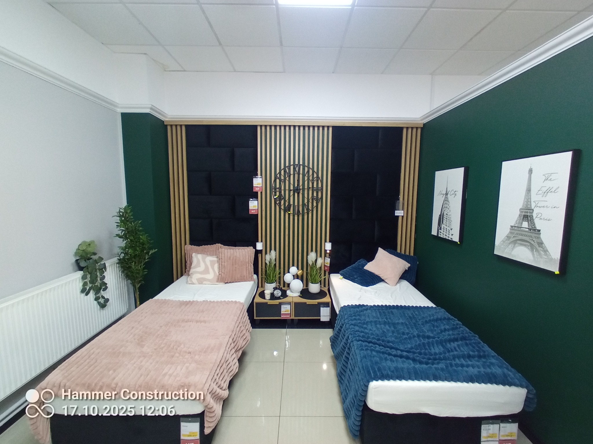 Dwa łóżka w pokoju z ciemnozielonymi ścianami i dekoracyjnym panelem za wezgłowiem. Na ścianach wiszą obrazy z motywami miejskimi. Nowoczesny design wnętrza.