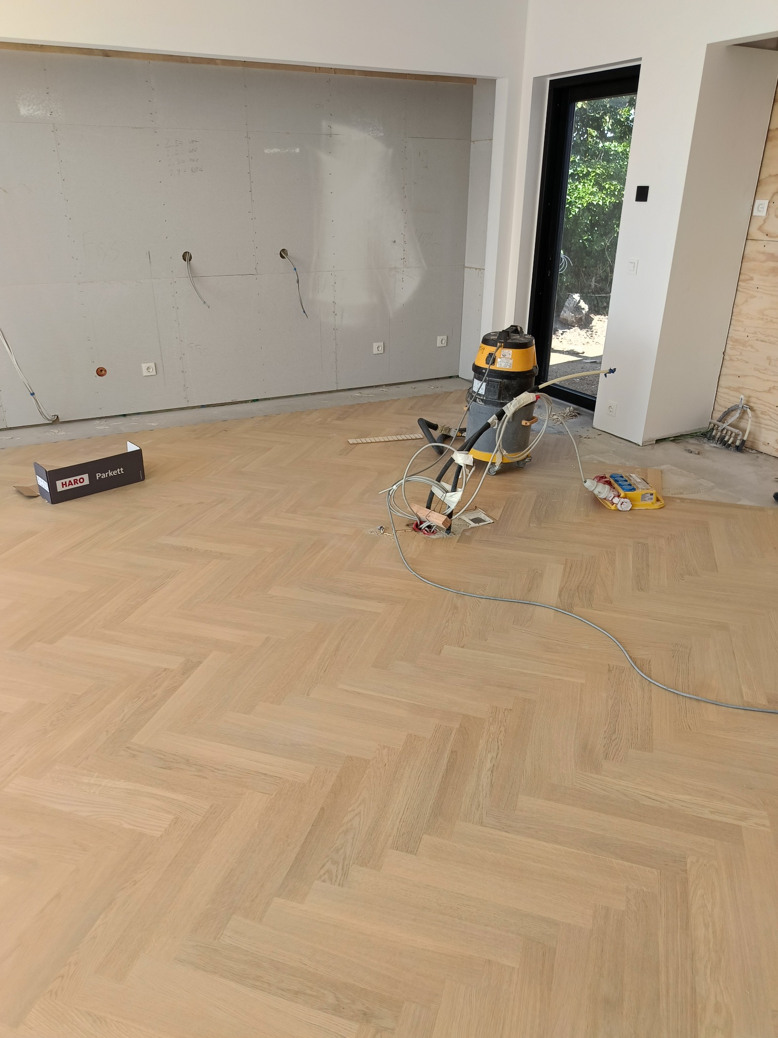 Ułożony parkiet w jodełkę w Sitkówce-Nowinach. Widoczne narzędzia pracy i karton po parkiecie. Ściany przygotowane do malowania. Jasne drewno, naturalne światło.