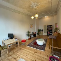 Paintpol - Jasne wnętrze pokoju z drewnianą podłogą i sztukaterią na suficie. Widoczne biurko, sofa, dywan i dekoracje. Ściany pomalowane na biało.