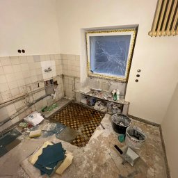 Paintpol - Wnętrze łazienki w trakcie remontu: zerwane płytki, odsłonięte instalacje, zabezpieczone okno folią, widoczne narzędzia i materiały budowlane. Stan surowy przed wykończeniem.
