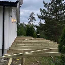 Paintpol - Konstrukcja drewnianego tarasu w trakcie budowy przy białym domu z numerem 9, widok z zewnątrz, narzędzia budowlane w pobliżu.