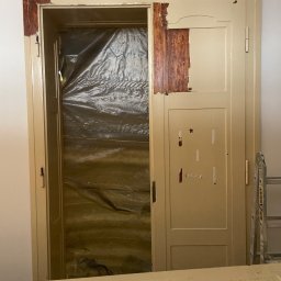 Paintpol - Przygotowanie do malowania futryny drzwiowej: częściowo usunięta stara farba, zabezpieczone folią wnętrze, widoczne ślady po taśmie malarskiej.