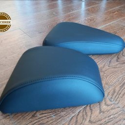 Dwa ciemnoniebieskie, tapicerowane siedziska o zaokrąglonym kształcie, leżące na drewnianej podłodze. Widoczne precyzyjne szwy i gładka powierzchnia materiału.