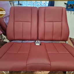 TAPICEREK JOLANTA KWOLEK-SOKÓŁ - Czerwone, skórzane siedzenia po renowacji tapicerskiej. Widoczne precyzyjne szwy i dbałość o detale. W tle warsztat tapicerski z narzędziami.