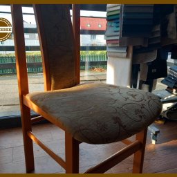 TAPICEREK JOLANTA KWOLEK-SOKÓŁ - Krzesło po renowacji tapicerskiej z wzorzystą tkaniną, widoczne próbki materiałów w tle. Drewniana konstrukcja krzesła w ciepłym oświetleniu.