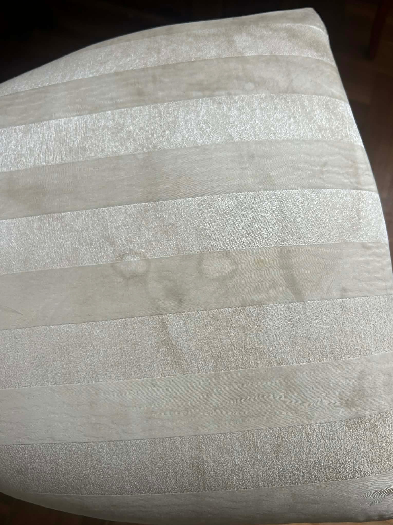 Fragment beżowego krzesła tapicerowanego w poziome pasy, z widocznymi plamami na środkowym pasie. Ujęcie z bliska, ukazujące strukturę materiału.