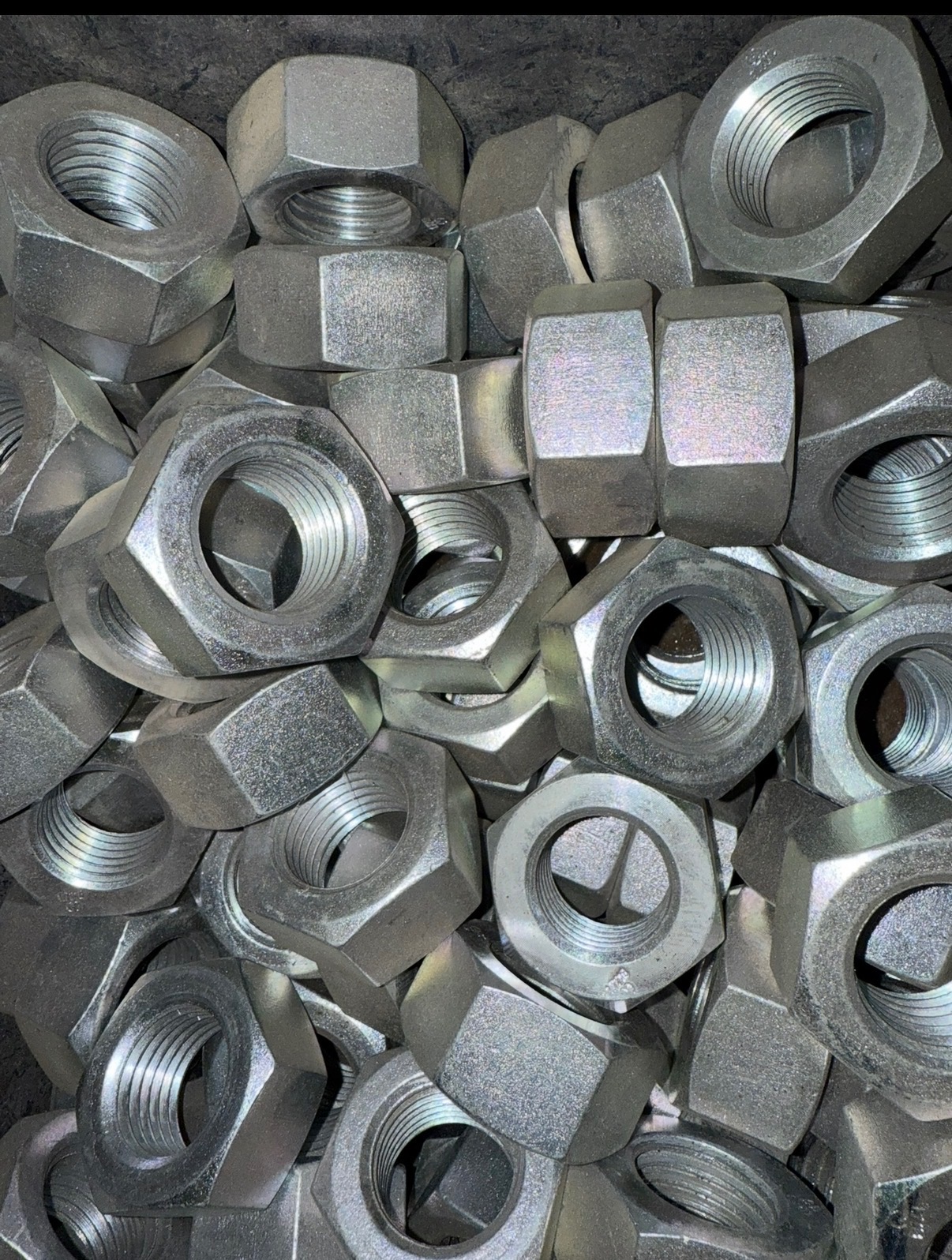 Stalowe nakrętki sześciokątne w dużym skupisku, widoczne gwinty i metaliczna powierzchnia, oświetlenie podkreśla detale obróbki.