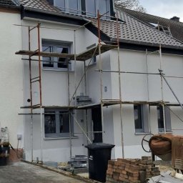 KPPS - Dom w trakcie prac elewacyjnych, widoczne rusztowania, świeżo pomalowana fasada w odcieniach szarości, przygotowane materiały budowlane i betoniarka.