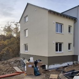 Trzykondygnacyjny budynek po ociepleniu elewacji, z widocznymi detalami wykończenia i przygotowanym terenem wokół. Częściowo otynkowana podmurówka.