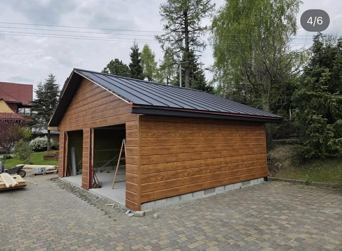 Nowoczesny garaż dwustanowiskowy z blachy trapezowej w kolorze antracytowym, wykończony drewnopodobną elewacją. Widoczne elementy konstrukcyjne i otoczenie.