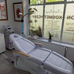 ANETT BEAUTY ANETA KRĘCICHWOST - Jasne wnętrze salonu kosmetycznego z białym fotelem zabiegowym, sprzętem kosmetycznym i dekoracjami. Na oknach grafika z nazwą salonu.