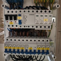 Denys Modelskyi 'DKSSystem' - Rozdzielnica elektryczna Schrack z bezpiecznikami i przewodami w kolorach: niebieskim, brązowym, żółto-zielonym. Widoczne oznaczenia Q1, Q2, Q3 oraz O1-O9.