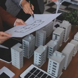 Lucyna Kwapińska - Analiza planu budynku z modelami wieżowców i turbin wiatrowych. Osoby wskazują na projekt, sugerując planowanie przestrzenne lub ocenę energetyczną.