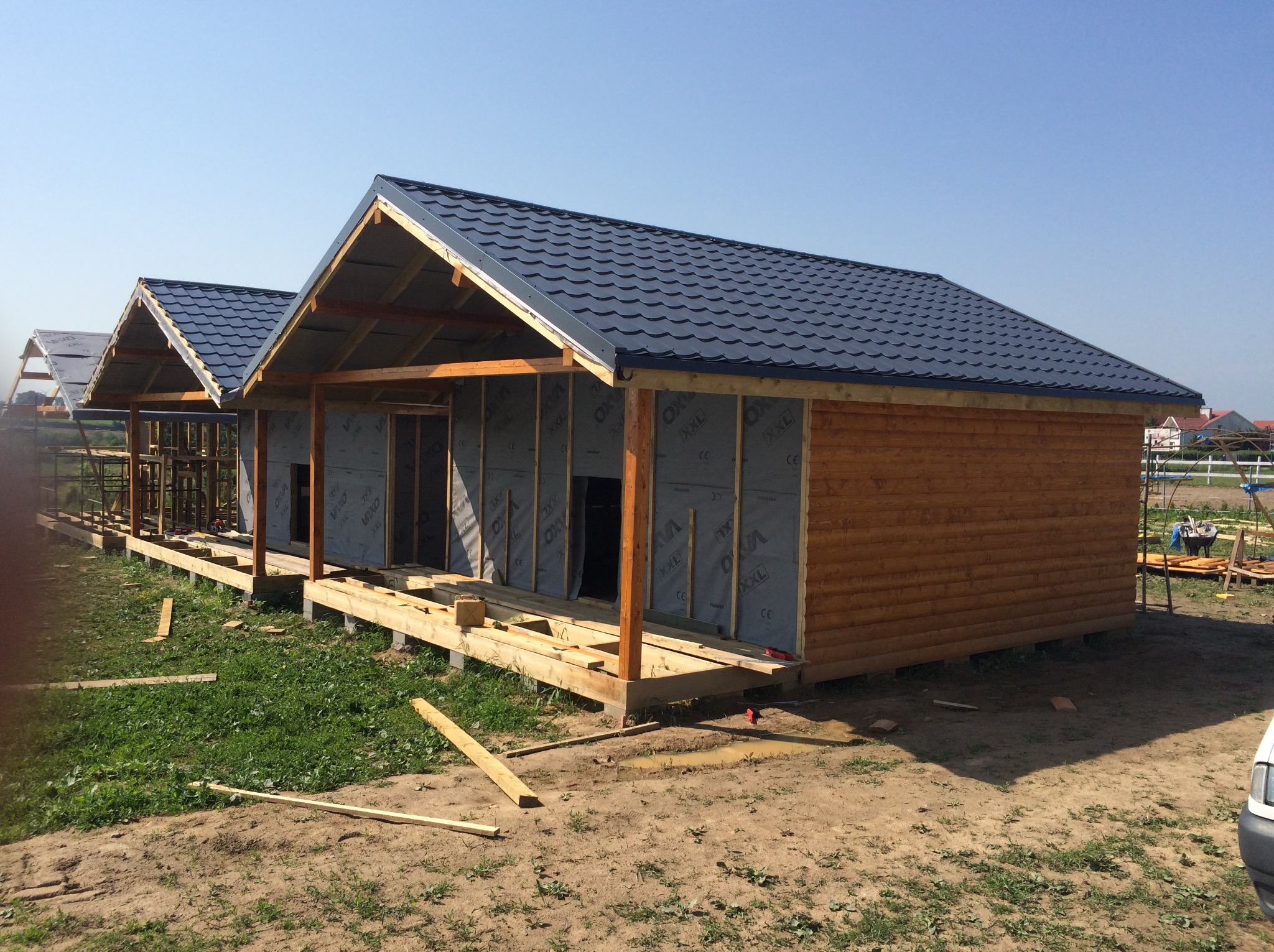 Wznoszenie domu szkieletowego: widok na konstrukcję z drewnianym szkieletem, częściowo obłożoną deskami i płytami izolacyjnymi, z ciemnym dachem z blachodachówki.