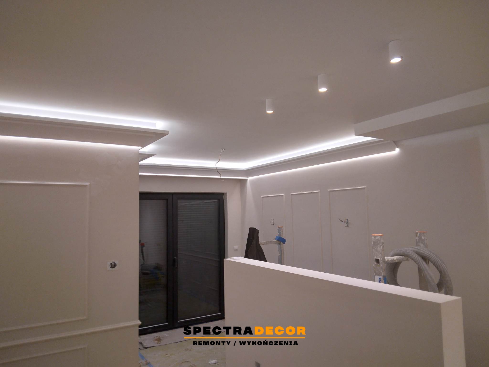 Wykończone wnętrze z dekoracyjnym oświetleniem LED na suficie i ścianach. Widoczne elementy sztukaterii i przygotowania do dalszych prac wykończeniowych.
