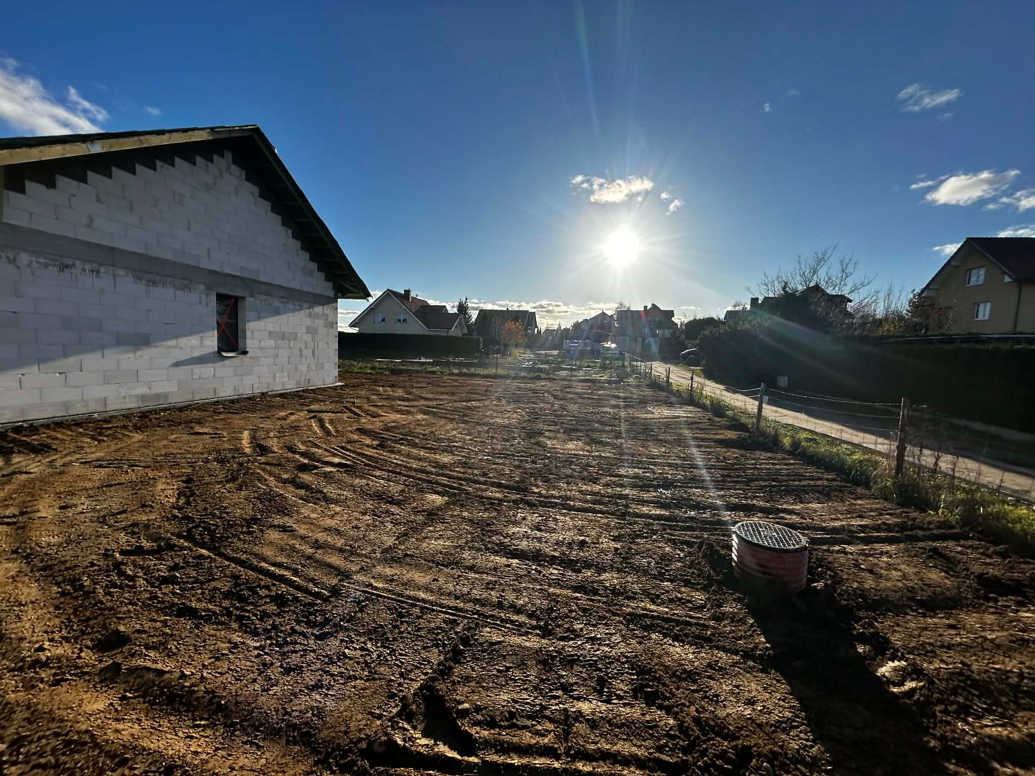 Przygotowany teren pod budowę domu jednorodzinnego z widocznymi śladami po maszynach budowlanych i studzienką kanalizacyjną w rogu działki.